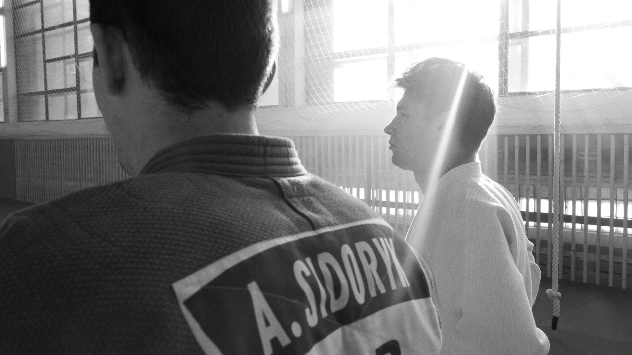 Black and white photo of two men practicing martial arts indoors with natural light.