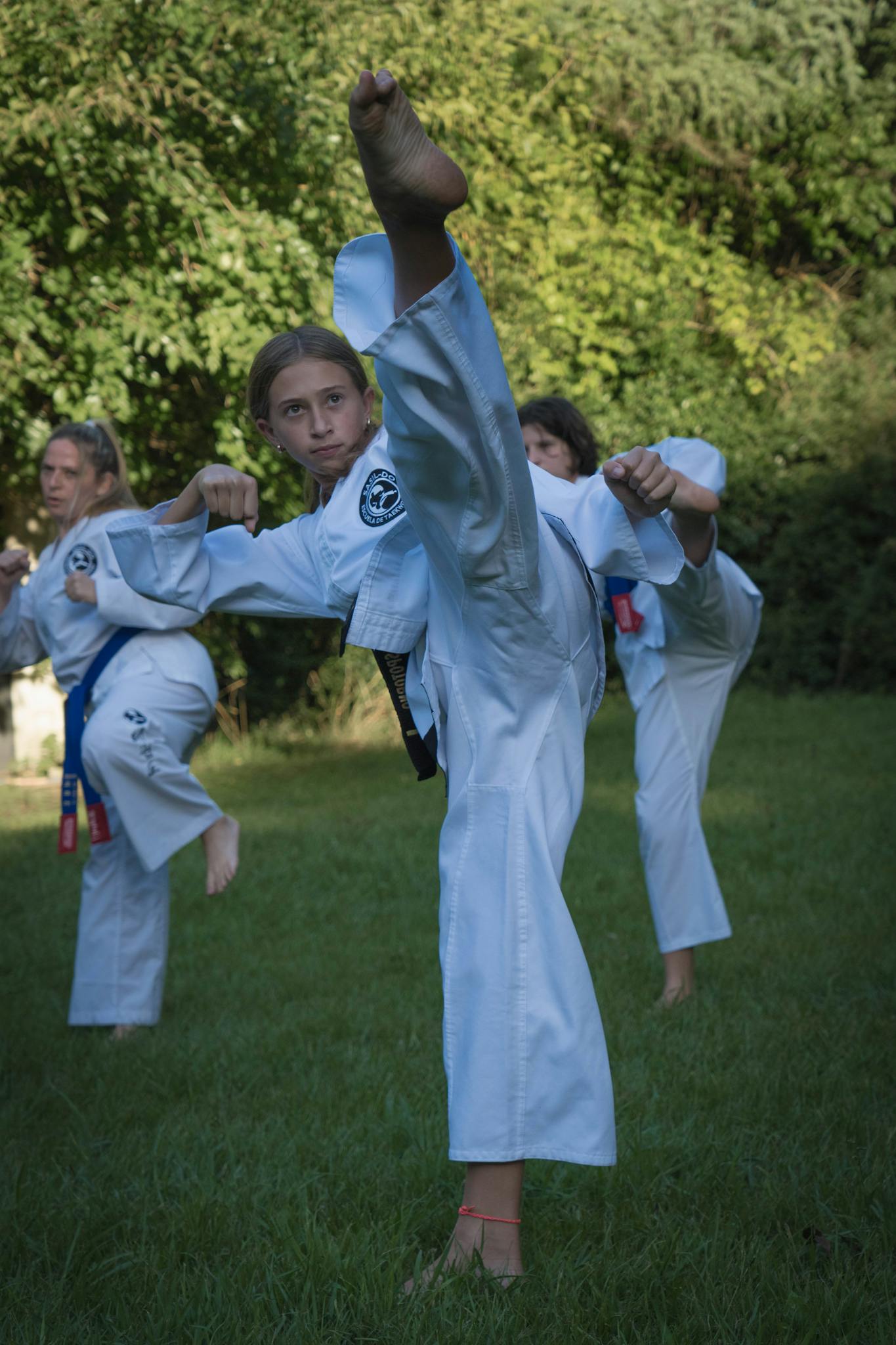 Young martial artists in uniform practicing kicks in a lush outdoor setting.
